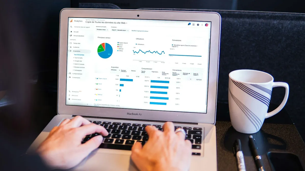 Mains sur le clavier d'un ordinateur portable affichant un tableau de bord Google Analytics, à côté d'une tasse