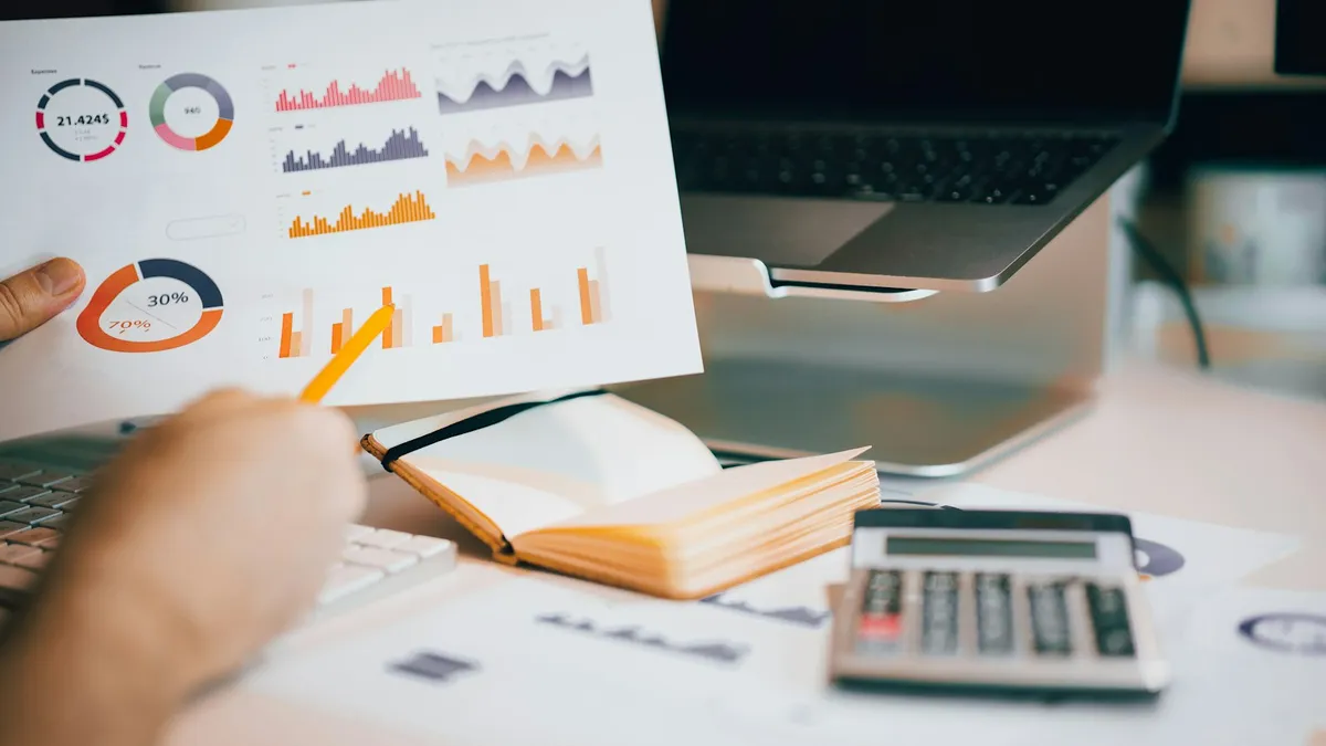 Main tenant une feuille de graphiques imprimés devant un ordinateur portable et une calculatrice